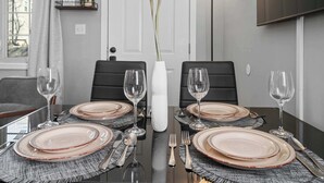 Una mesa de comedor dispuesta con platos, vasos, cubiertos y un jarrón con flores.