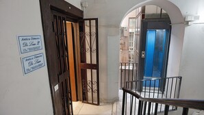 A staircase with a metal railing, a wooden door with a decorative metal gate, and a blue elevator door. - Antica Dimora Deluxe with Balcony, Wi-Fi and Air Conditioning (Napoli)