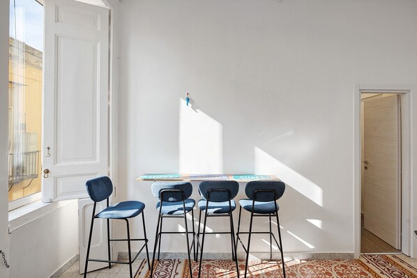 A room with a white door, a window, a table with chairs, and a patterned rug.