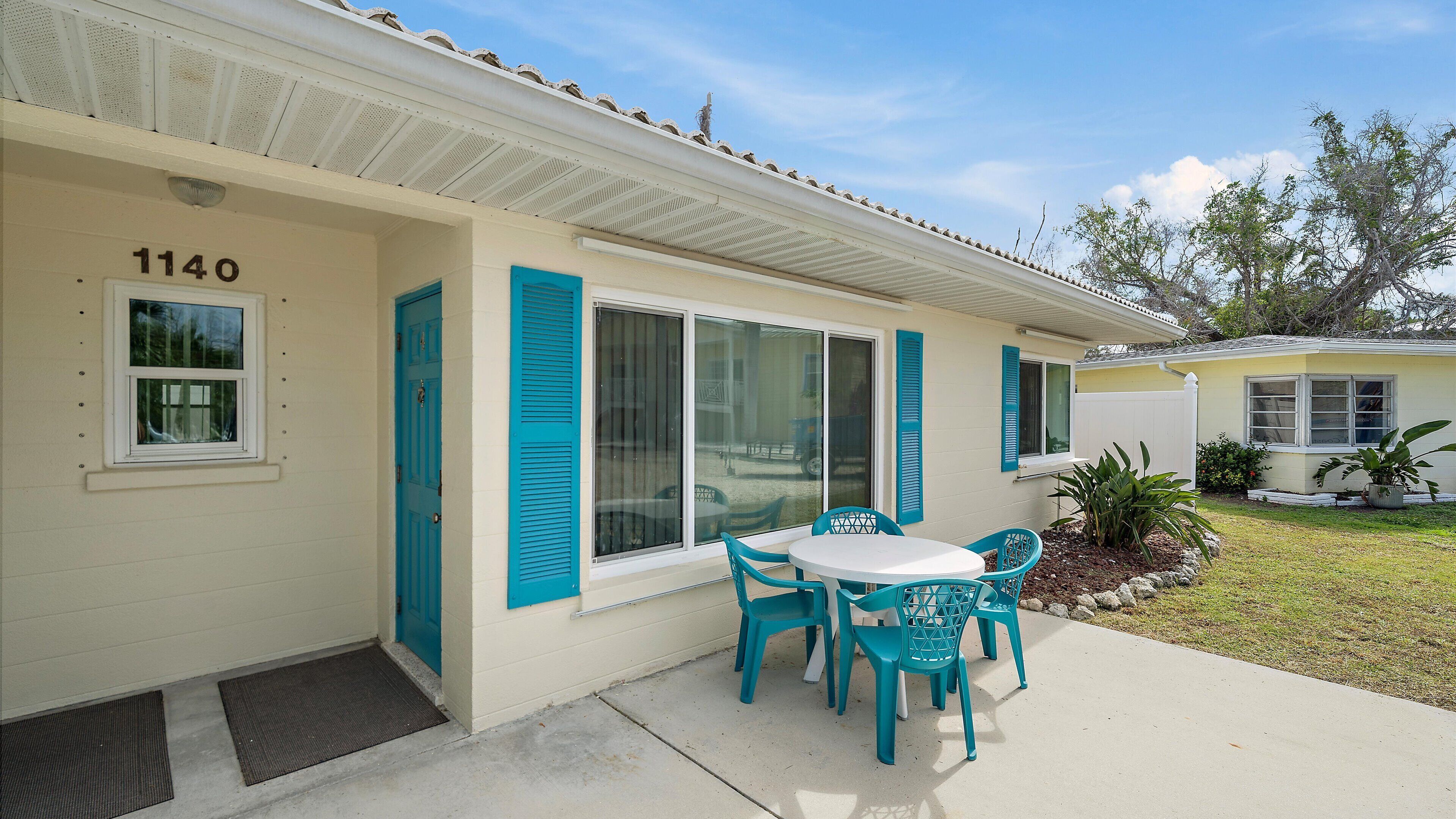 A house with a number 1140 on the wall, a patio with a table and chairs, and a small garden area.