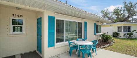A house with a number 1140 on the wall, a patio with a table and chairs, and a small garden area.