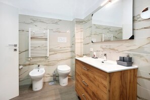 Un bagno moderno con bidet, WC, lavabo e specchio.