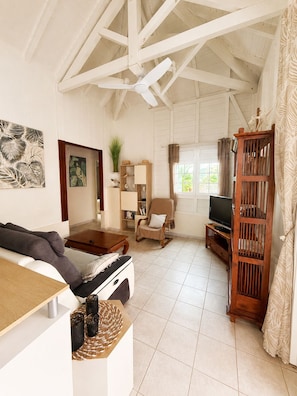 A living room with a sofa, a coffee table, a TV stand, a rocking chair, and a wooden bookshelf. - Villa Ti Gîte 3*** Bougainvillier (Le Marin)