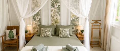 A bedroom with a canopy bed, two bedside tables with lamps, a wooden chair, and a window with curtains.