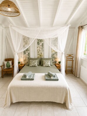 A bedroom with a canopy bed, two bedside tables with lamps, a wooden chair, and a window with curtains. - Villa Ti Gîte 3*** Bougainvillier (Le Marin)