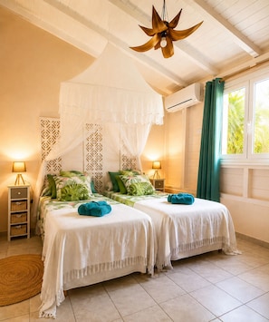 A bedroom with two beds, a canopy, a ceiling fan, bedside lamps, and a window with curtains. - Villa Ti Gîte 3*** Bougainvillier (Le Marin)