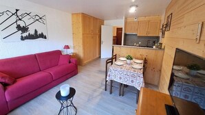 Un espacio habitable compacto con un sofá rojo, una mesa de comedor para cuatro personas y una cocina con armarios de madera.