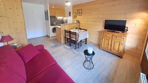 Un espacio habitable compacto con kitchenette, comedor, televisi ón y un sofá rojo.