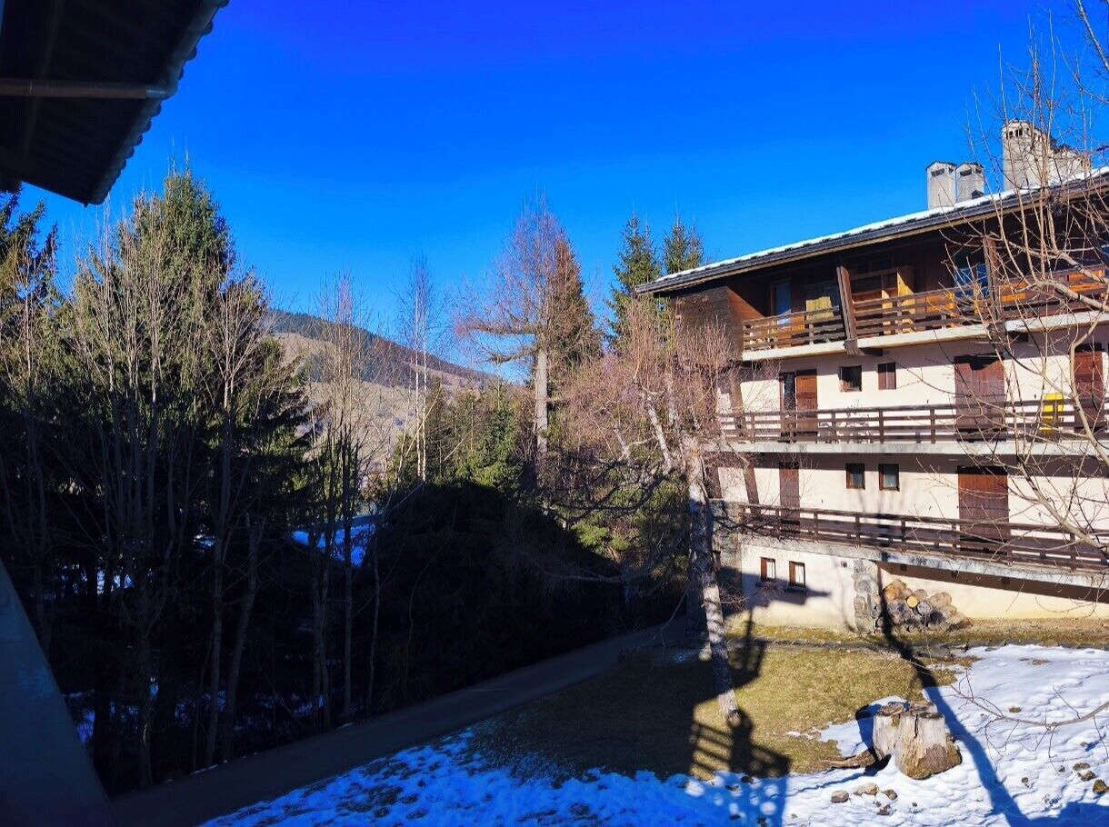 A traditional chalet with a wooden balcony, surrounded by trees and a clear blue sky.