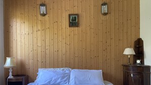 Ein Schlafzimmer mit einer holzgetäfelten Wand, einem Bett mit weißer Bettwäsche, zwei Wandlampen und einem kleinen Gemälde über dem Bett.