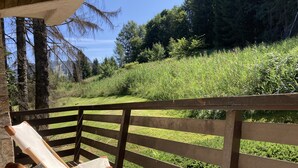 Eine Holzterrasse mit einer Bank und einem Tisch, mit Blick auf einen grasbewachsenen Hang mit Bäumen.
