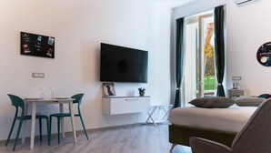 Une chambre d’hôtel moderne équipée d’un lit, d’une télévision, d’une table à manger avec des chaises et d’une fenêtre avec des rideaux.