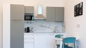 Une cuisine compacte avec des meubles gris, un four à micro-ondes, une machine à café et un petit coin repas avec des chaises de couleur turquoise.