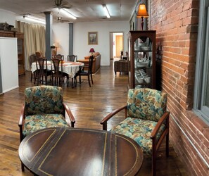 Uma sala de jantar com cadeiras de madeira e uma mesa redonda, uma parede de tijolos e uma estante com louças.