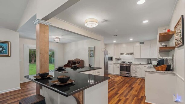 A modern kitchen with white cabinets, a black countertop island, and a wooden floor. - Magnolia Retreat 4BR 3BA Home (Hattiesburg)