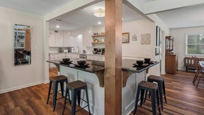A modern kitchen with a central island, bar stools, and a dining area with a wooden table and chairs. - Magnolia Retreat 4BR 3BA Home (Hattiesburg)