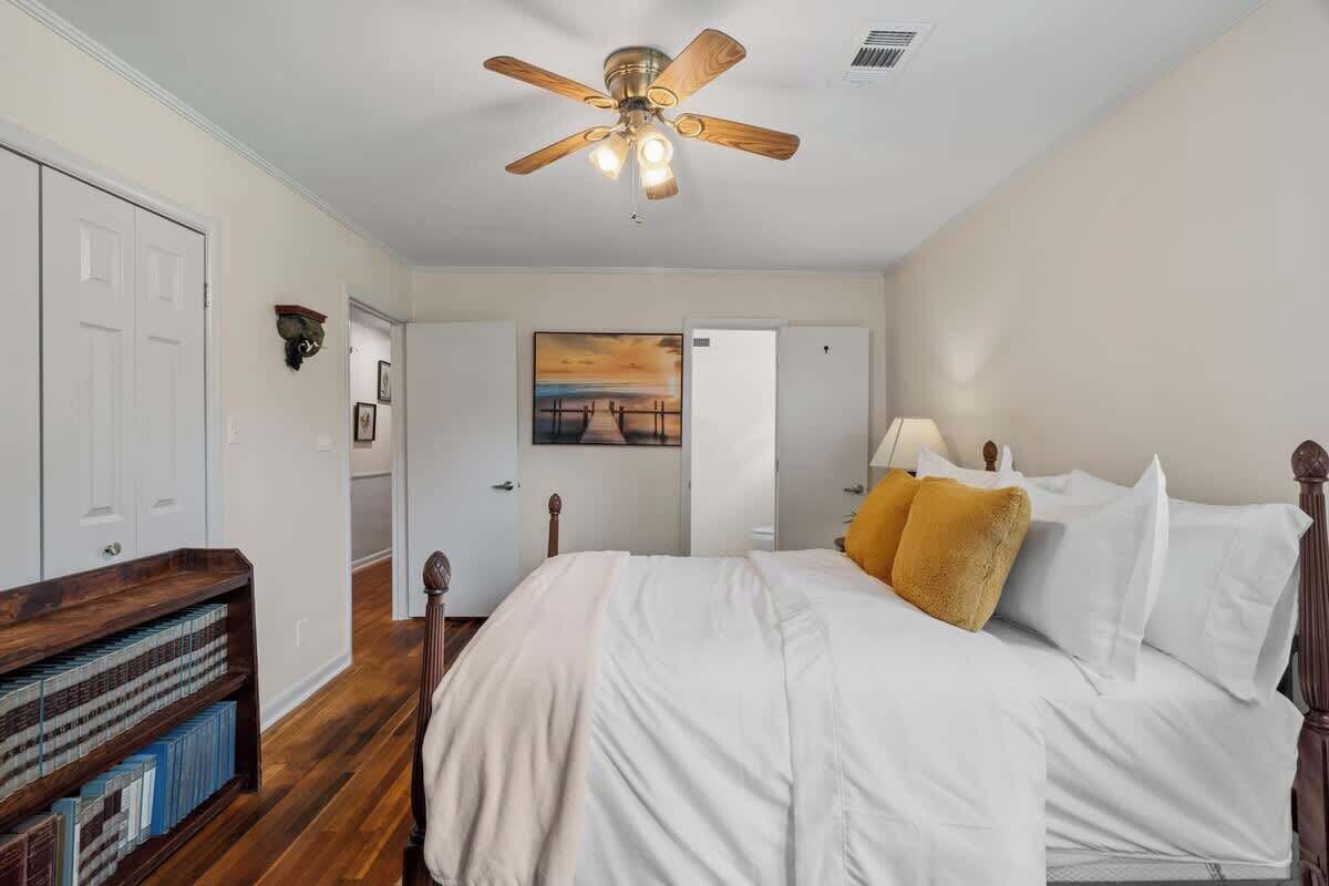 A bedroom with a bed, a ceiling fan, a bookshelf, and a painting on the wall.