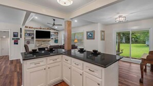 A modern kitchen with white cabinetry, a black countertop, and a central island. There is a ceiling fan, recessed lighting, and a view of the outdoors through large windows. - Magnolia Retreat 4BR 3BA Home (Hattiesburg)