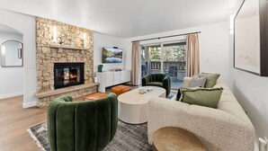 Un salon moderne avec une cheminée en pierre, un téléviseur, un canapé et un balcon aménagé avec des sièges d’extérieur.