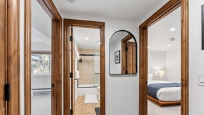 Une chambre d’hôtel avec un plancher en bois, un lit recouvert d’une couverture bleue, un mur blanc et un grand miroir.