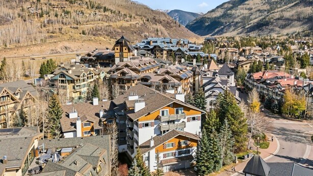 Une ville de montagne où se côtoient des bâtiments traditionnels et modernes, entourée de collines boisées et dominée par un ciel dégagé.