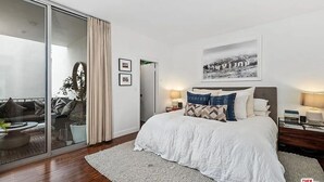 Quarto com uma cama grande, porta de vidro que dá para uma varanda e um quadro na parede.