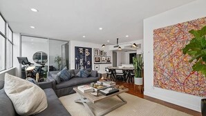 Uma sala de estar moderna com um sofá cinza, uma mesa de centro e um grande quadro abstrato na parede.