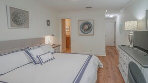 Een slaapkamer met een groot bed, nachtkastjes, een dressoir, een televisie en kunst aan de wanden.