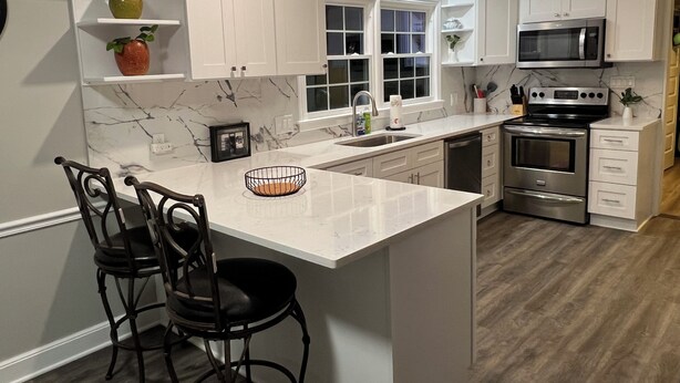 A modern kitchen with white cabinetry, a marble backsplash, a central island with bar stools, and stainless steel appliances.