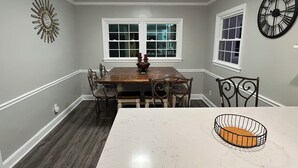 A dining room with a wooden table, chairs, a chandelier, and a clock on the wall.