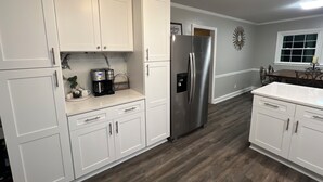 A modern kitchen with white cabinets, a stainless steel refrigerator, and a coffee maker.