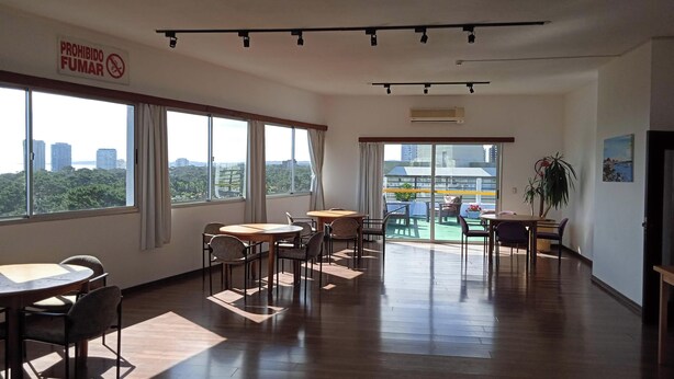 A spacious room with multiple tables and chairs, large windows offering a city view, and a balcony with outdoor seating. - Charming 1 and a half-bedroom apartment in beautiful Punta del Este. 4 people (Punta del Este)
