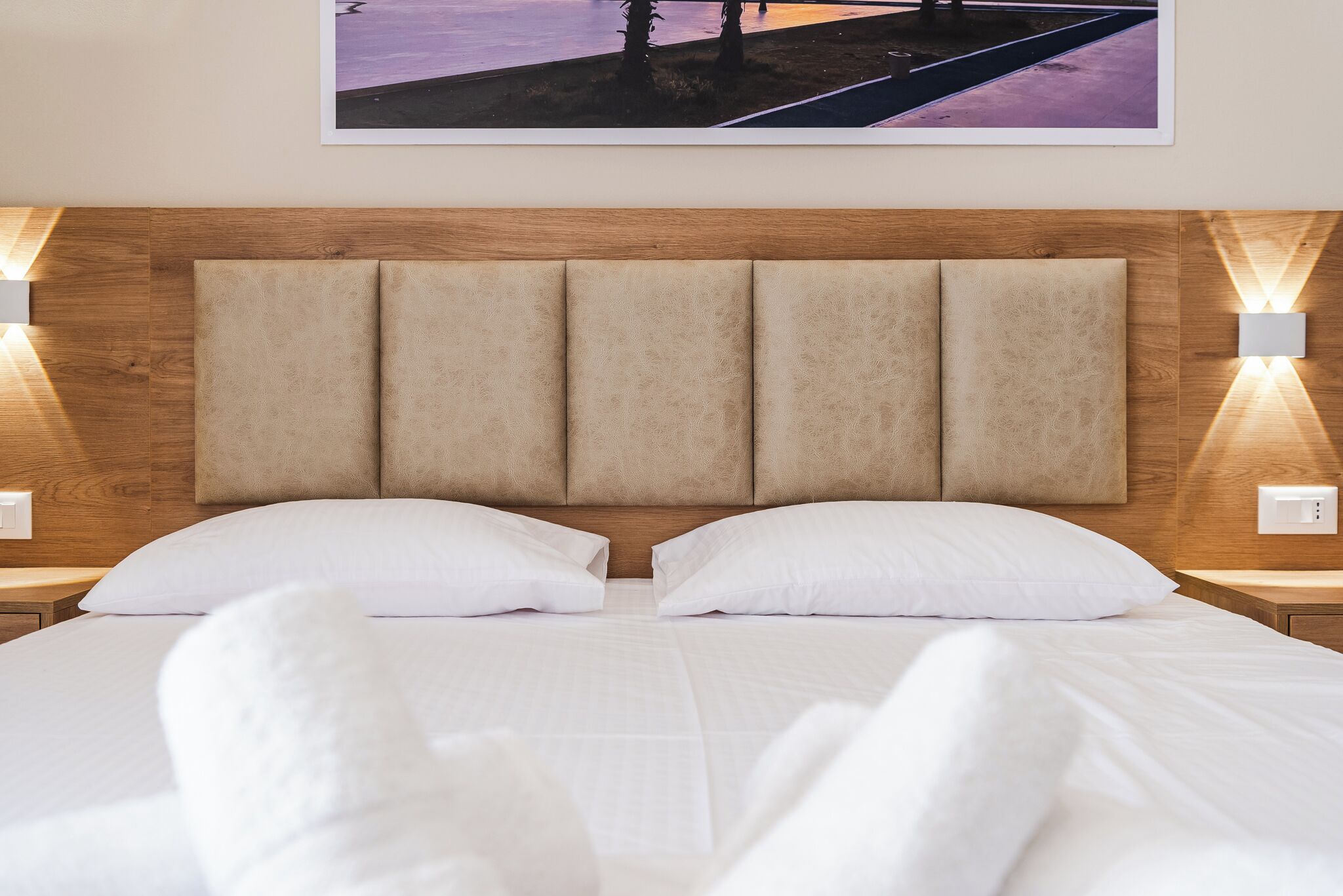 Ein ordentlich bezogenes Bett mit weißen Leinen und Kissen, ein Holz-Kopfteil sowie zwei Wandleuchten.