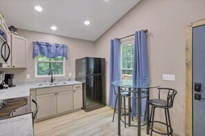 Cocina compacta con refrigerador, pileta y una mesa de vidrio con dos sillas.