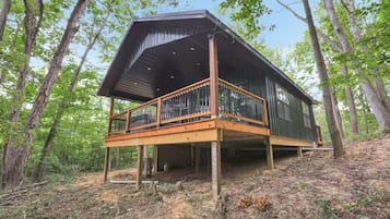 A cabin with a wooden deck and a metal roof, surrounded by trees.