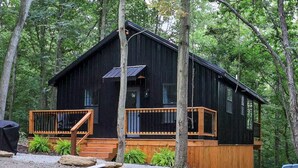 Une cabane dotée d’une terrasse en bois, d’un petit porche et d’un panneau solaire sur le toit.