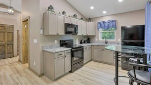 Une cuisine moderne avec des meubles de couleur bois clair, une cuisinière en acier inoxydable, un four à micro-ondes et une table à manger en verre, accompagnée de chaises.
