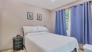 Une chambre à coucher avec un lit, une table de chevet, une fenêtre avec des rideaux et deux tableaux encadrés accrochés au mur.