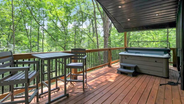 Une terrasse couverte avec un jacuzzi, des meubles en bois et une vue sur une forêt.