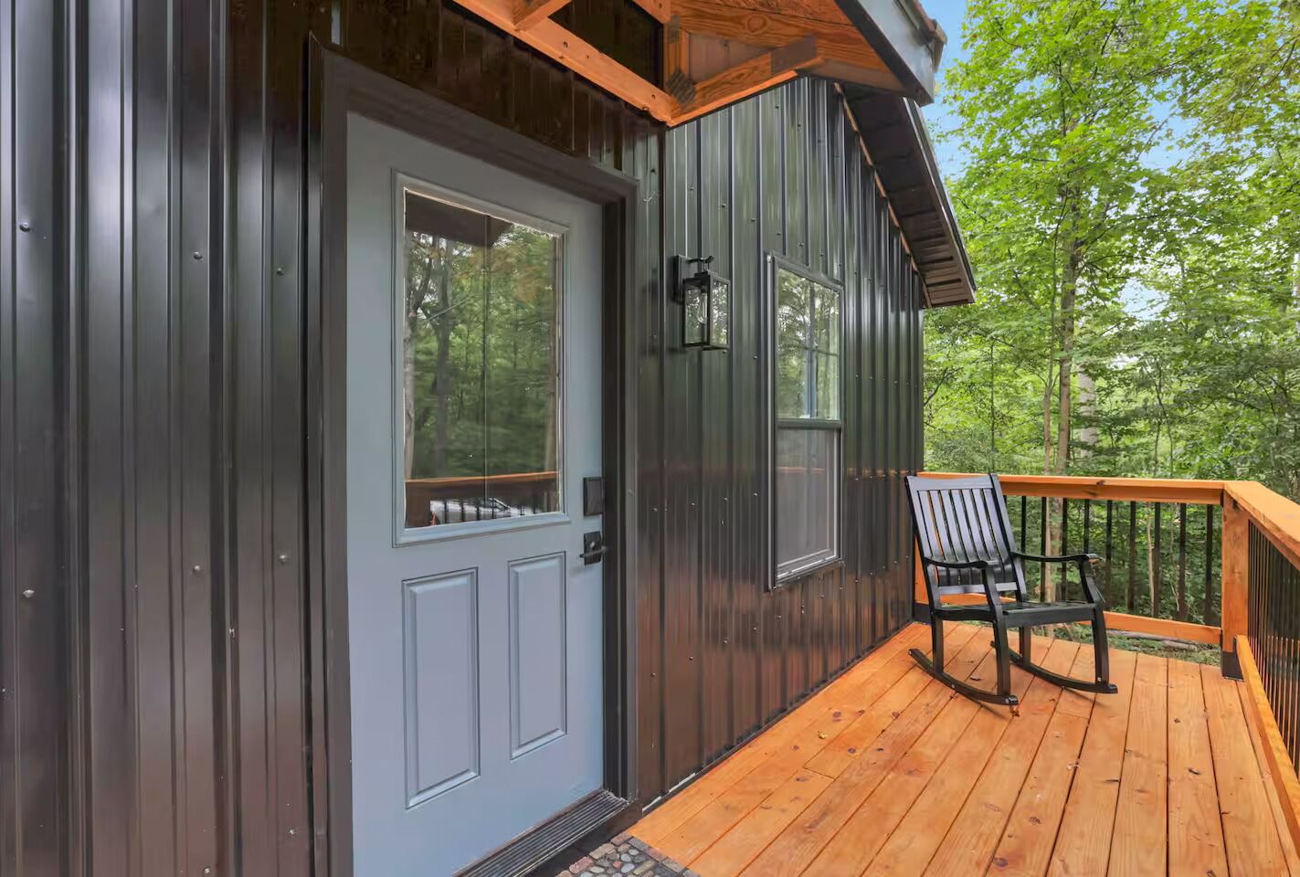 A wooden deck with a bench, a gray door with a window, and a metal exterior wall.