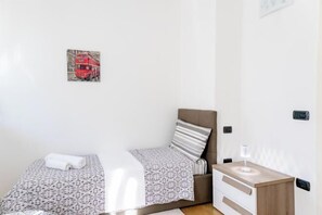 A small, clean room with a bed, a bedside table, and a wall-mounted light. - Charming Two Bedroom Apartment (Venice)