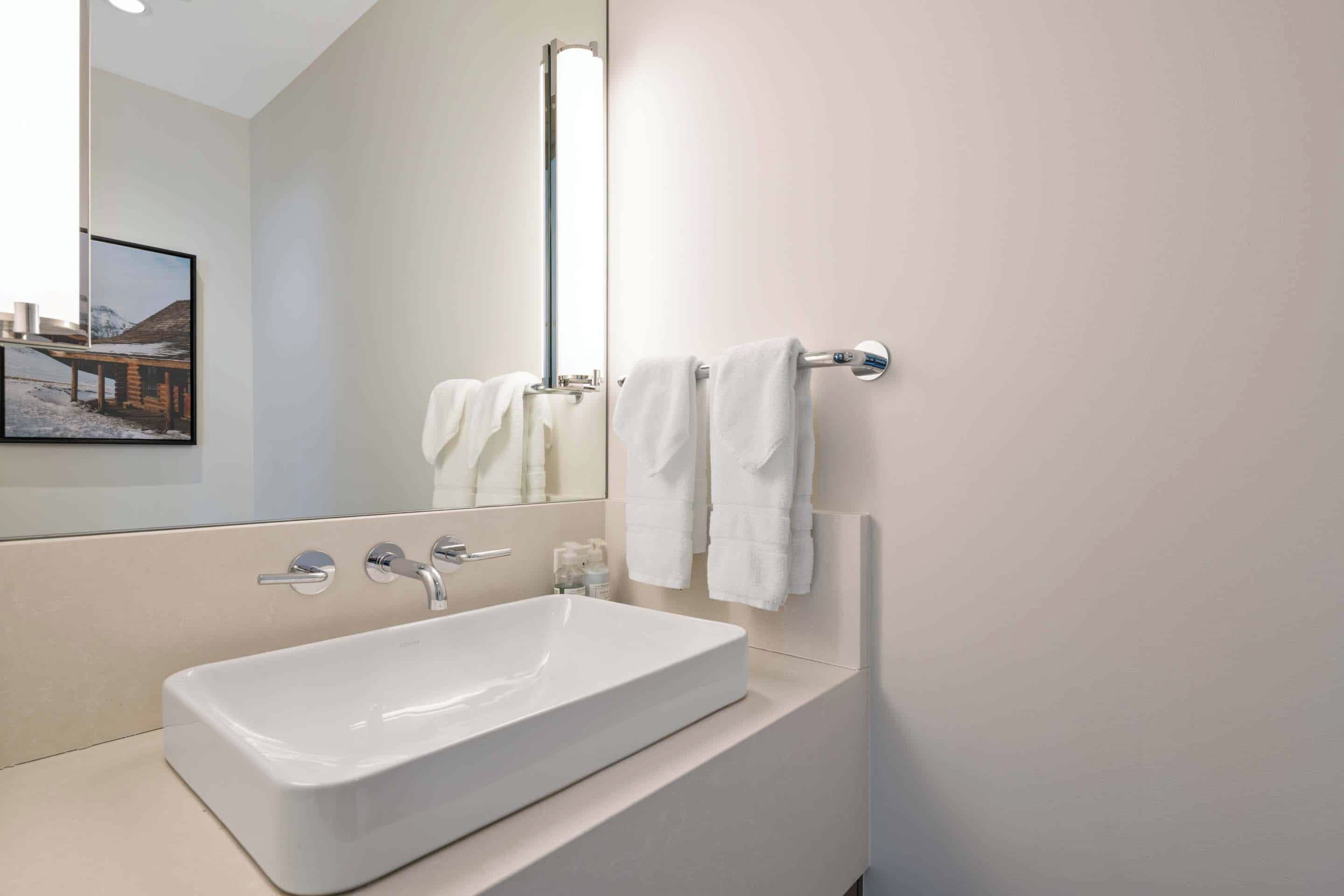Une salle de bain moderne avec un grand lavabo rectangulaire, un miroir et deux serviettes suspendues à un porte-serviettes.