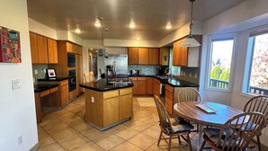 A modern kitchen with wooden cabinets, a central island, and a dining area with chairs. - Columbia View Retreat, Spacious Furnished Home in Argay Terrace,Portland Airport (Portland)