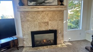 A living room with a fireplace, a flat-screen TV, and a large window with a view of trees. - Columbia View Retreat, Spacious Furnished Home in Argay Terrace,Portland Airport (Portland)