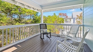 En inglasad veranda med en gungstol och två solstolar, med utsikt över ett skogsområde och ett hus.