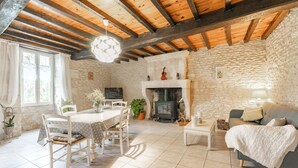 A rustic room with a stone wall, wooden beams, a fireplace, a dining table with chairs, a sofa, and a television.