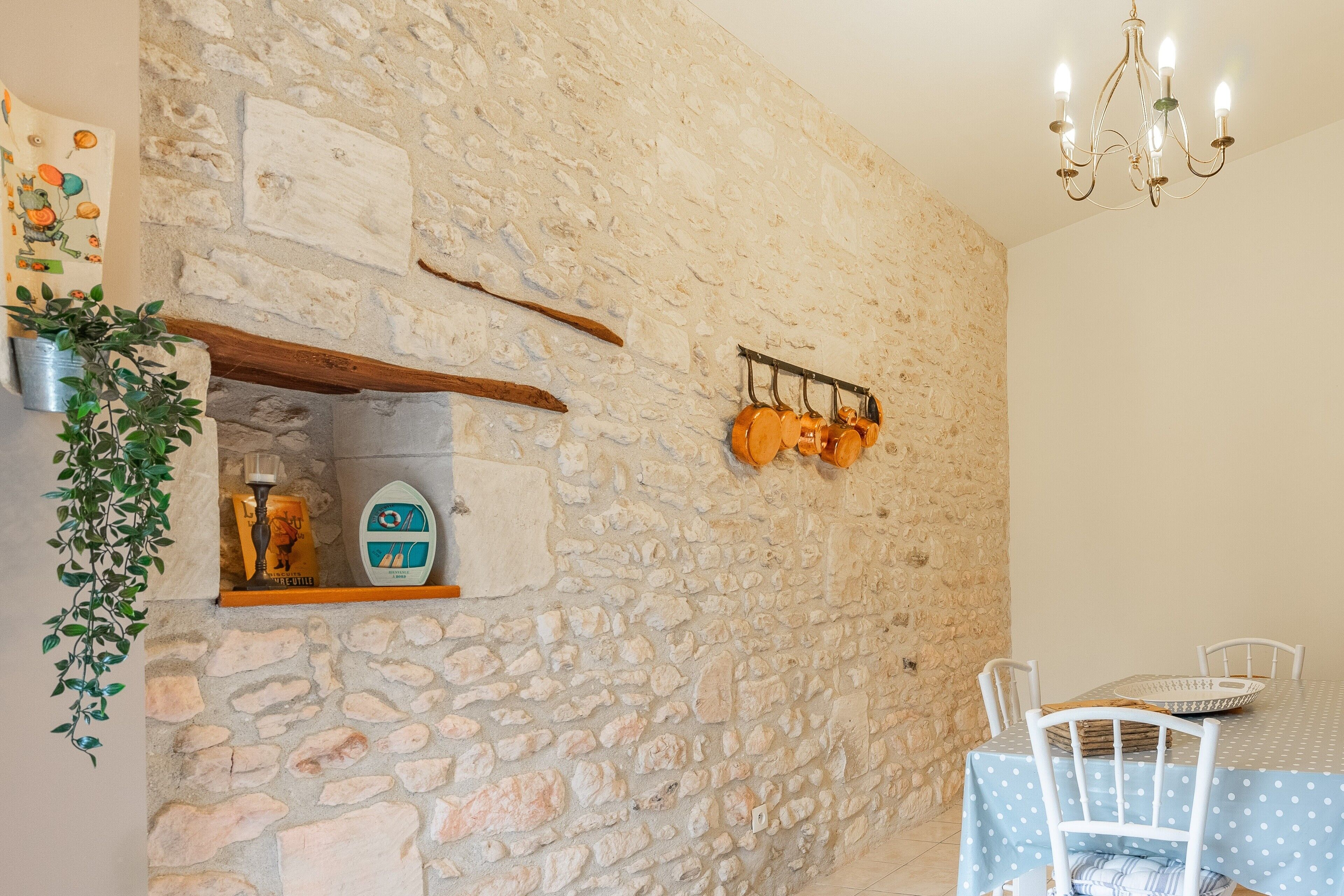A stone wall with a hanging pot rack, a table with chairs, and a chandelier.
