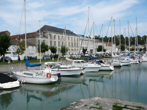 Un port de plaisance où sont amarrés de nombreux bateaux, un grand bâtiment en arrière-plan et une surface d’eau calme.