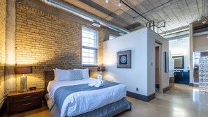 Une chambre d’hôtel moderne avec un mur en briques, un grand lit décoré d’un cygne, une table de chevet et une lampe.