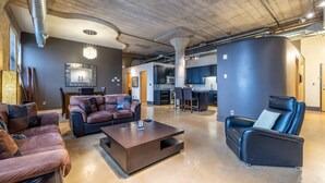 Un vaste espace de vie avec des canapés en cuir, une table basse et une cuisine en arrière-plan.